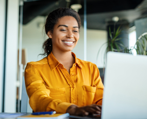 Happy Black Businesswoman Using Laptop Typing And Working Online While Sitting At Workplace In Office